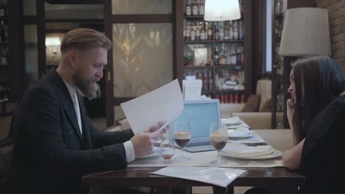 Brunette Woman and Blond Bearded Man Sitting at the Table in the Cafe Working and Drinking Beer
