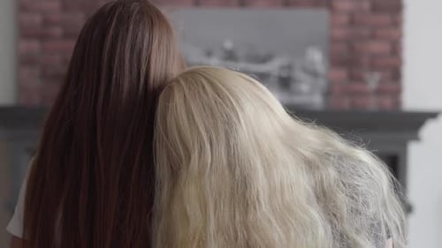 Back View of Two Girls with Long Beautiful Hair Sitting Near Each Other in the Living Room. Concept