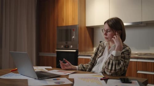 A Pensive and Tired Woman with Glasses Working on Financial Documents Sitting in the Workplace Using