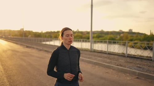 Woman Running Across Bridge During Sunrise or Sunset