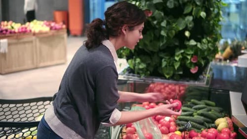 Young Beautiful Brunette Girl in Her 20's Picking Out Tomatoes Into a Plastic Bag at the Fruit and