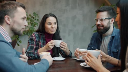 Cheerful Men and Women Chatting and Laughing Drinking Coffee in Cozy Cafe