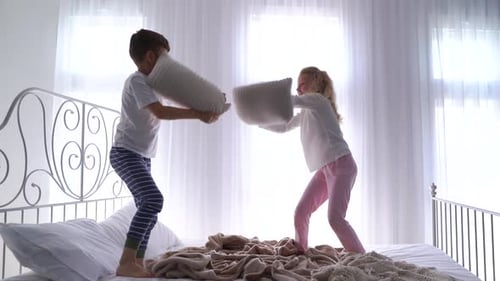 Deux enfants tenant un oreiller se battant s'amusant ensemble en jouant dans le lit Chambre moderne confortable
