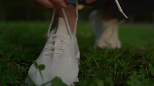 Close-up view of unrecognizable young woman tying shoelaces on sneakers before running.