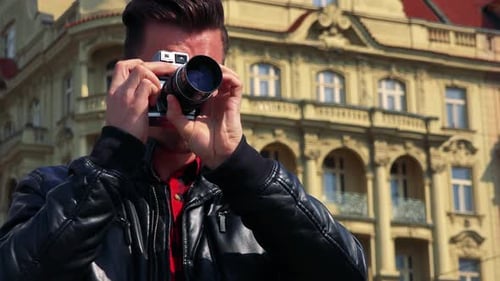 A Young Handsome Man Takes Photos with a Camera - Closeup From Below - an Old Yellow Building