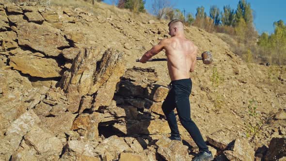 Shirtless bodybuilder splitting rocks with a sledgehammer. Strong man ...