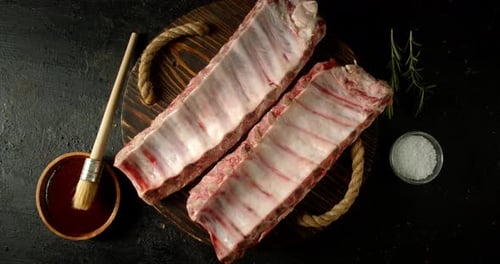 Raw Ribs Rotate Slowly on a Wooden Tray.