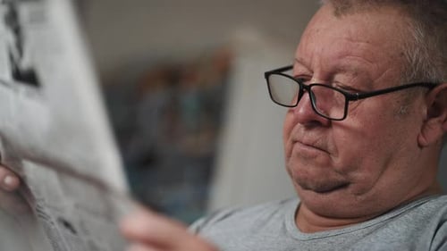 Senior Man Reading Newspaper Indoors, Close Up