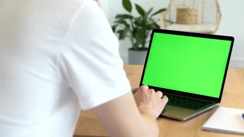 Over the shoulder shot of a man typing on a computer laptop with a key-green screen
