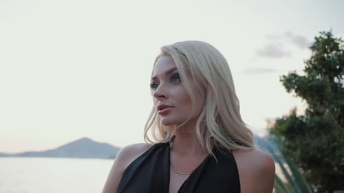 Beautiful blonde woman in black dress walking at sunset against the sea