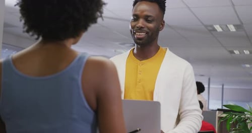 Happy african american male and female business colleagues talking in office