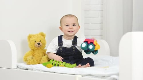 Baby Sits With Toys on White Bed