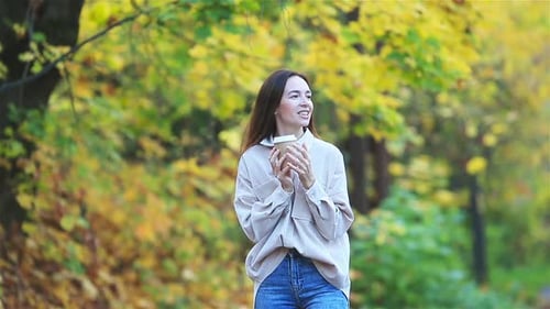 Beautiful Woman Drinking Coffee in Autumn Park Under Fall Foliage