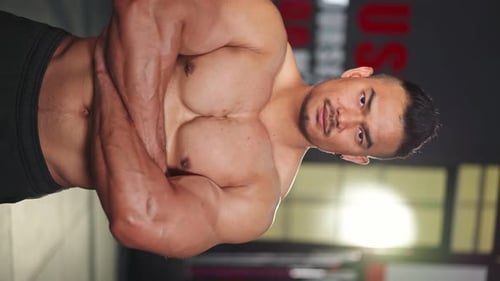 Vertical Portrait of Shirtless Asian Active bodybuilder showing physical form, muscle in fitness gym