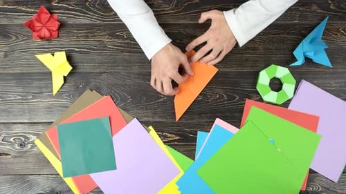 Mann faltet Papierblätter, während er Origami macht.