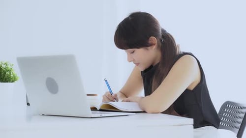 Beautiful asian woman smiling sitting in the living room study and learning writing notebook.