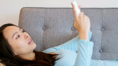 Woman Using Smartphone Relaxing on Couch Indoors
