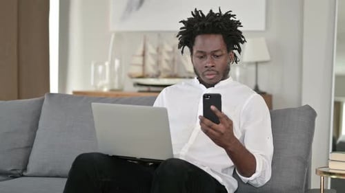 Young Adult on Couch Using Laptop and Smartphone