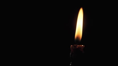 Une seule bougie est allumée sur fond noir. Flamme de bougie dans le noir.