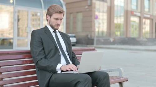 Man Working on Laptop Sitting on Park Bench