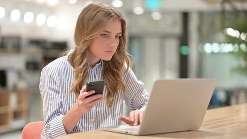 Businesswoman with Laptop Using Smartphone in Office