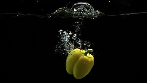 Gelbe Paprika fällt ins Wasser und dreht sich mit vielen Luftblasen und Tröpfchen