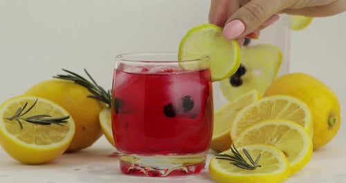Zitronenscheibe in ein Glas mit Roter Limonade-Cocktail geben