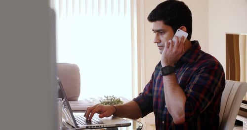 Young Adult Works on Laptop While Talking on Phone