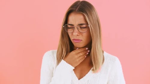 Young Lady Has a Sore Throat and Coughing Looking Unhappy and Sick While Posing Against Pink Studio