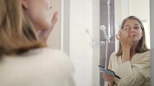 Woman Applying Makeup in Bathroom Mirror