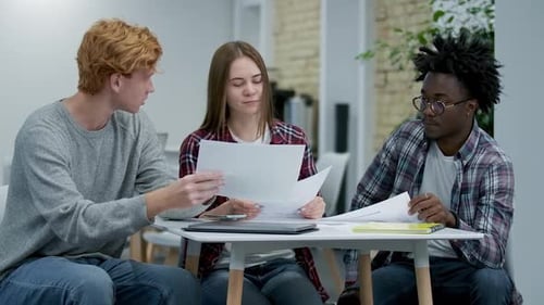 Three Young Concentrated Coworkers Examining Papers in Office. Portrait of Confident Caucasian and