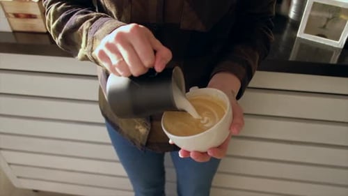 Close up barista hands pouring warm milk in coffee cup for making latte art.