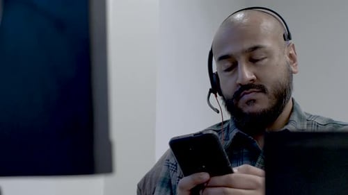 Close up shot of an Asian call centre employee taking a break from calls while sitting at his workst