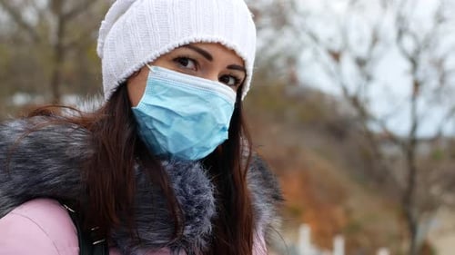 A woman with long dark hair in a mask from air pollution and the Covid19 coronavirus walk
