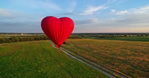 Hot air balloon flying over field. Romantic red aerostat in the heart shape moving slowly in the air