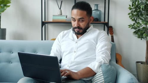Adult Man Works On Laptop On Couch Indoors