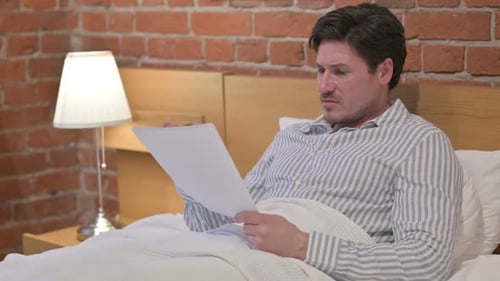 Man Reviews Paperwork in Bed, Discards Documents