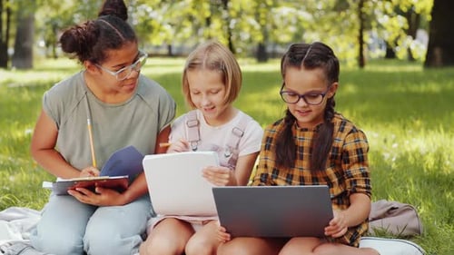 Cute Multiethnic Schoolgirls Using Laptop and Studying in Park