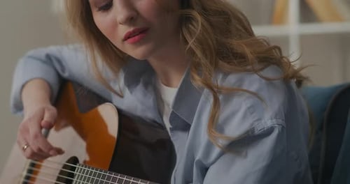 Woman Playing Acoustic Guitar Indoors on Couch