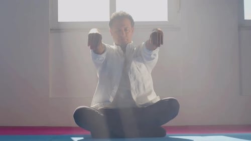Man Meditating and Raising Arms in Bright Room
