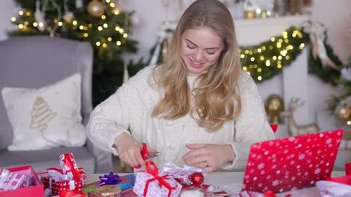 Woman Happily Wrapping Christmas Presents with Red Ribbon