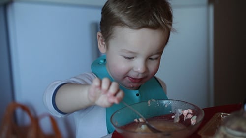 Happy Child Eating Lunch at Home with Parent