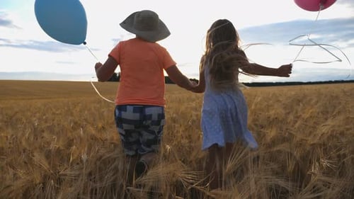 Small Girl and Boy Holding Hands of Each Other and Running Among Barley Plantation. Couple of Little