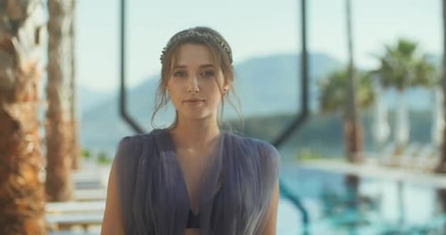 Young lady standing over the pool and looking at camera on holidays.