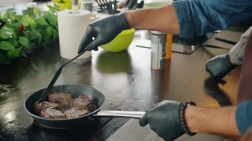 Close-up of Male Cook Making Meat Dish in Frying Pan on Cooker in Kitchen