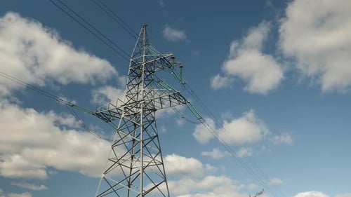 Power line against blue sky with clouds at windy sunny day. High-voltage tower and wires, timelapse