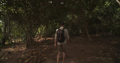 Dolly Shot Following a Male Tourist with Backpack Hiking Through the Jungle in Bali on a Dirt Path