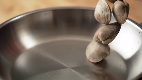 La caméra suit la cuisson des palourdes dans une poêle. Ralenti.