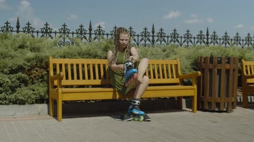 Teenager Lacing Up Roller Blades on Park Bench