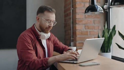 Freelancer Sitting at the Cafe and Typing Something at the Laptop with Smile